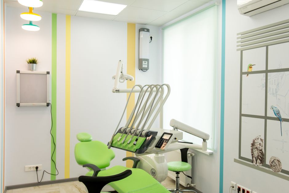 A bright treatment room with a green dental chair, pastel stripes on the wall and a window with soft light