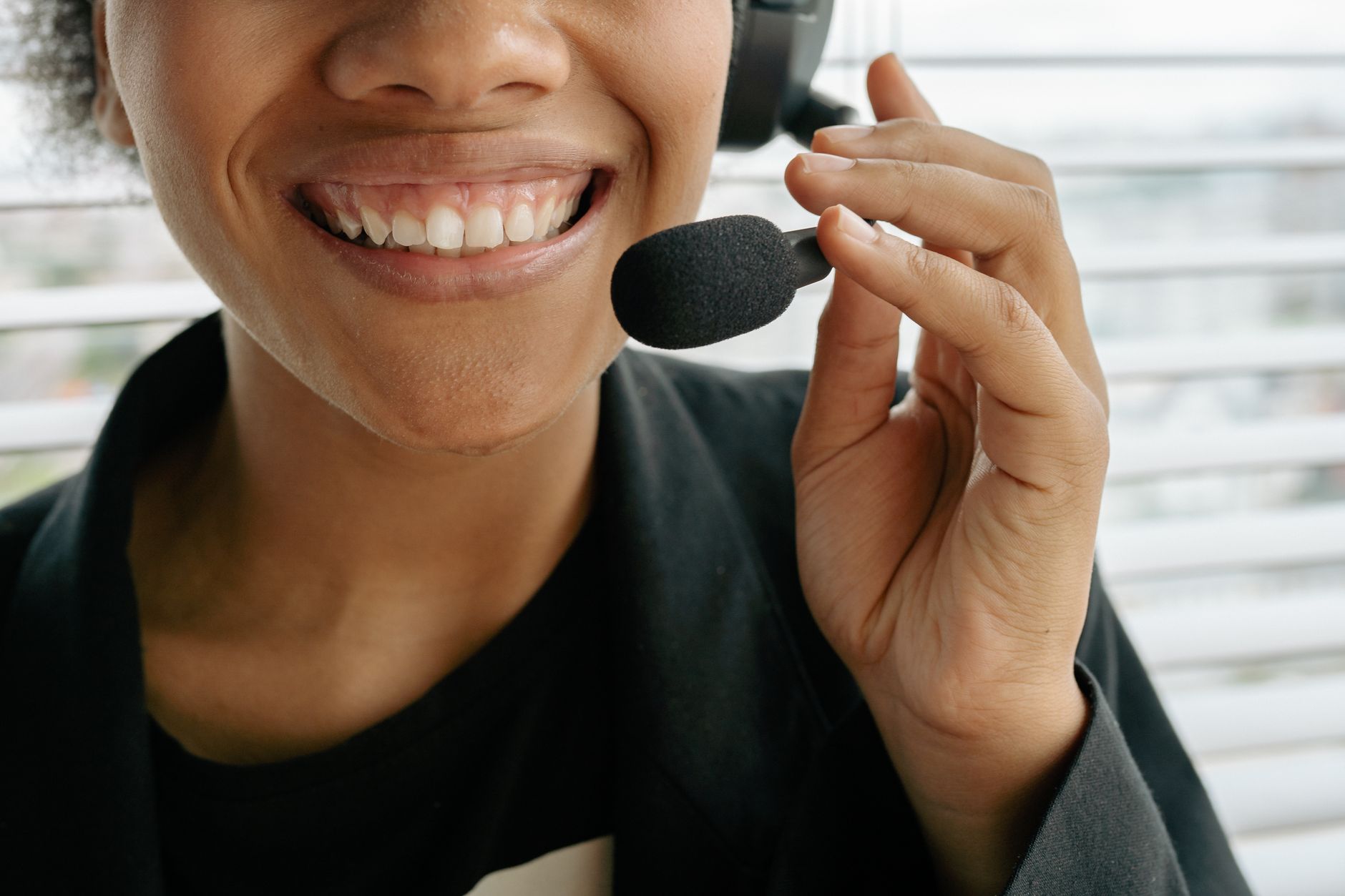 Close-up of a smiling person wearing a headset with the microphone raised toward their mouth