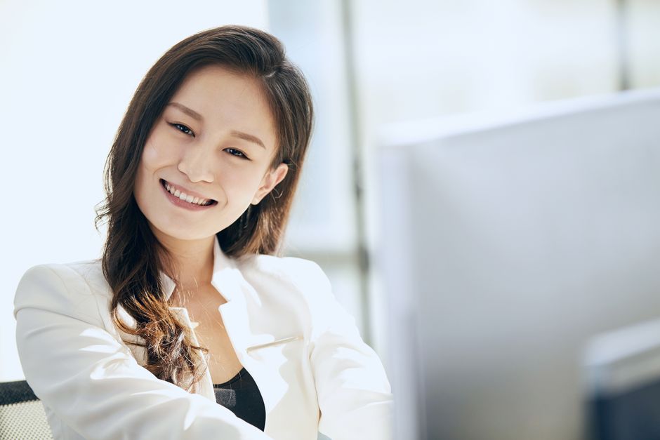 A smiling woman in a white blazer looking at the camera in a bright office