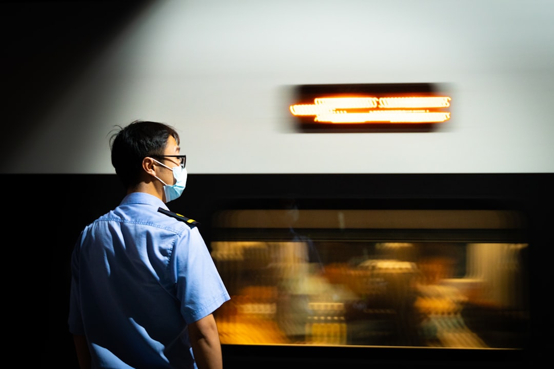 A man wearing a face mask standing in front of a train